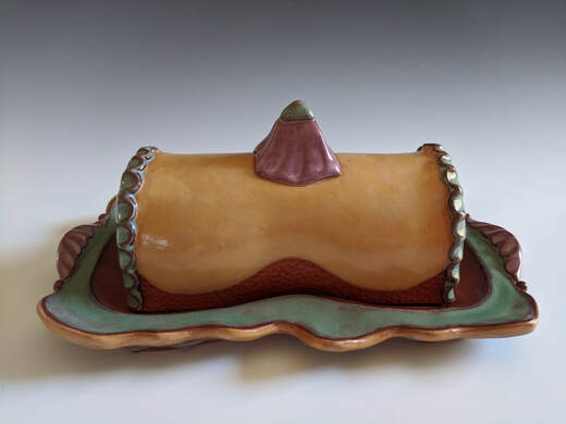 A pottery butter dish in caramel and sage green glazes with pyramid knob on top